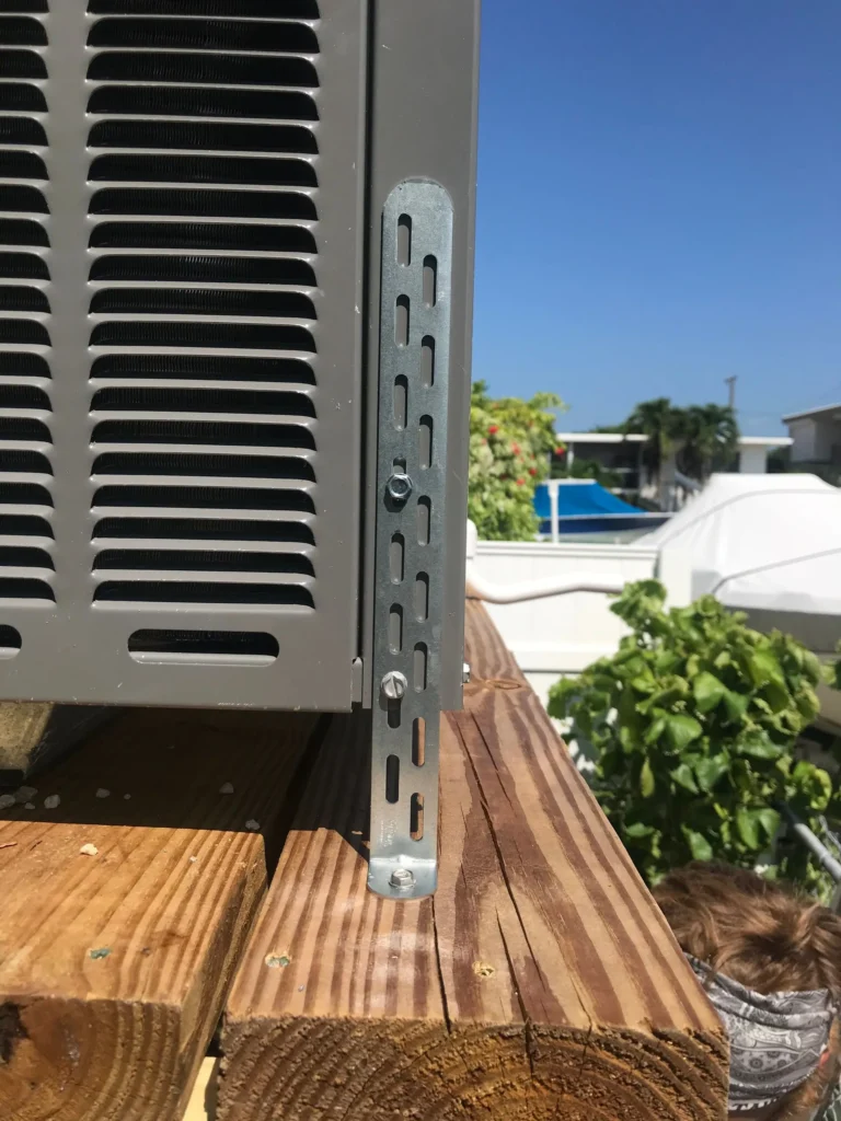 Hurricane tie-down bracket securing an outdoor AC unit to its platform