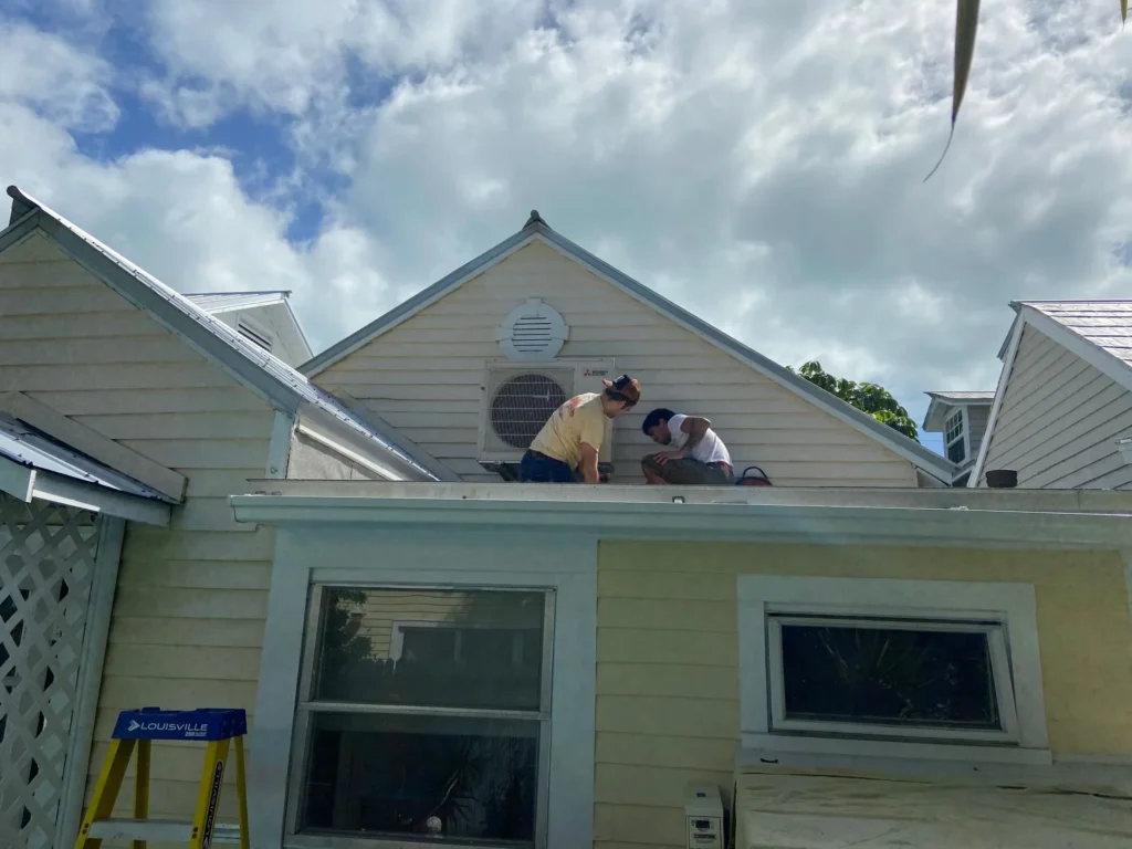 Two Cool Aid technicians installing a ductless mini-split condenser on a rooftop gable