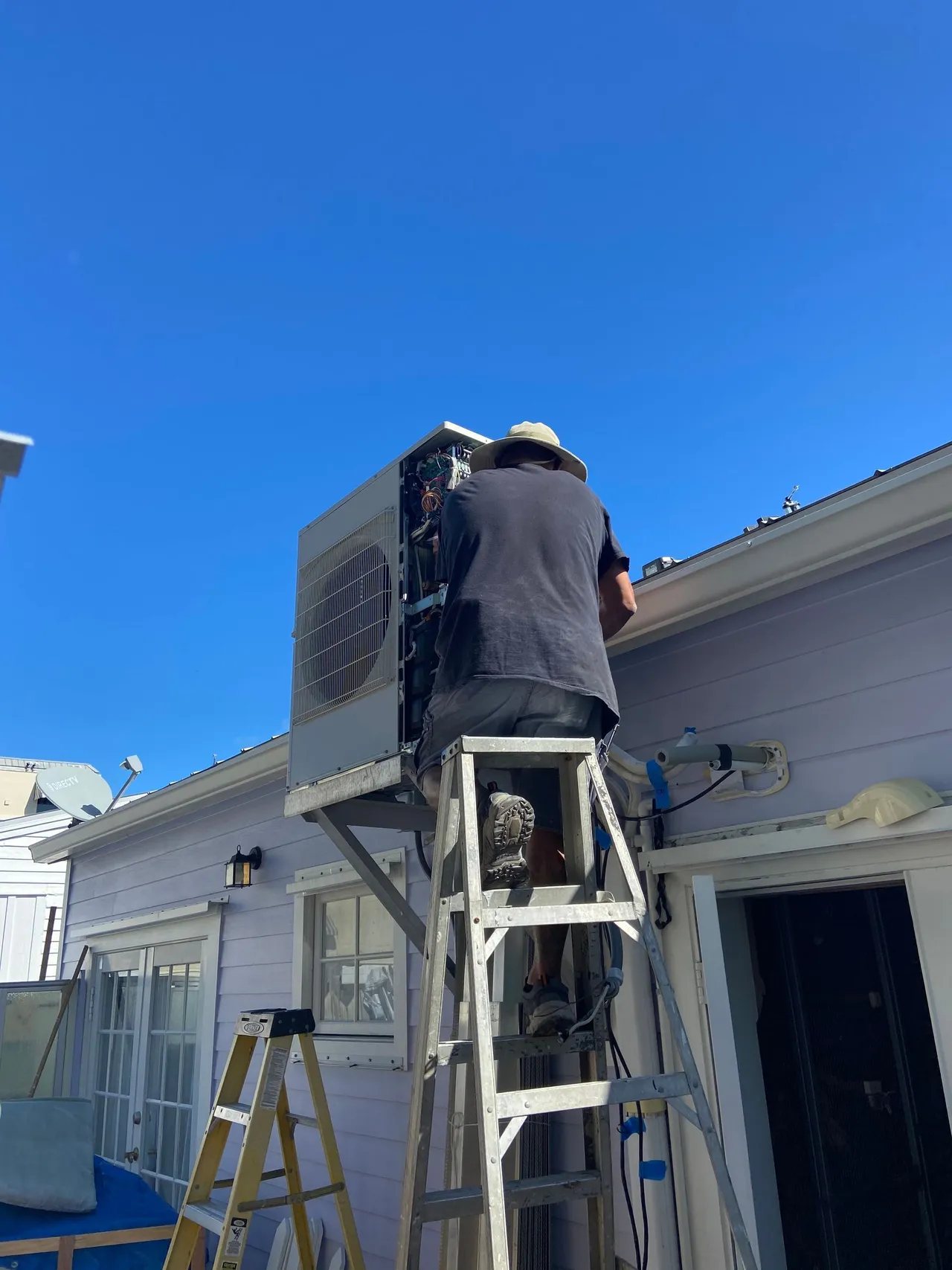 Cool Aid technician on a ladder servicing a wall-mounted mini-split condenser
