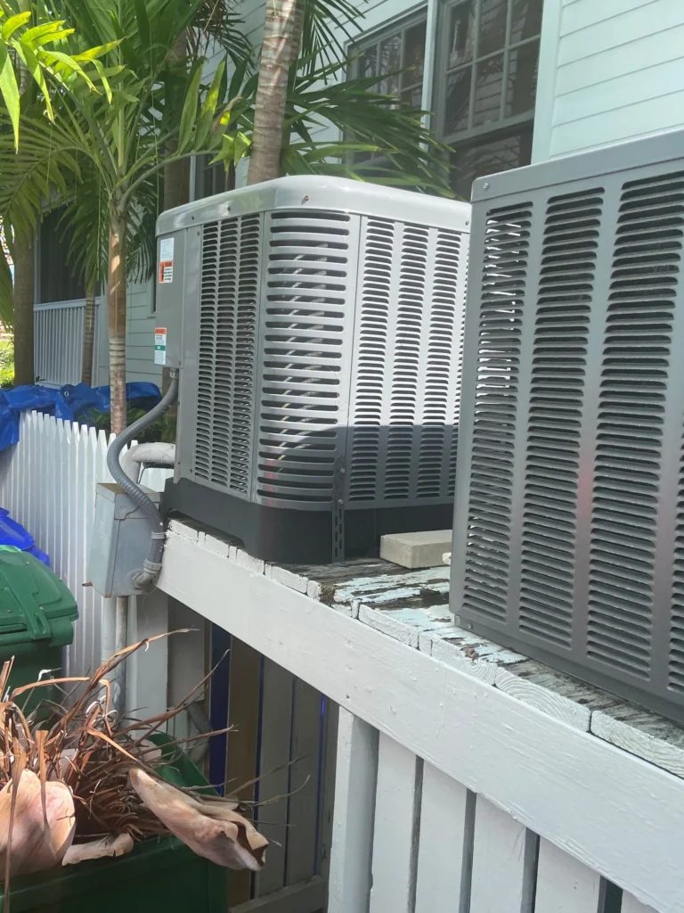 Two condensing units installed side by side on a raised platform under palm trees